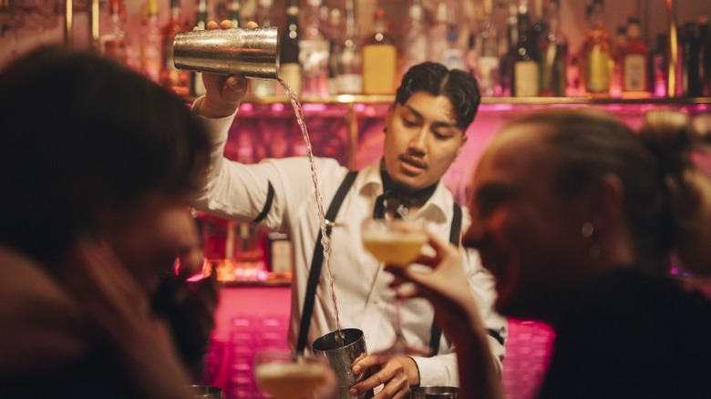 Bartender makes drink in background while couple talks at bar in the foreground.