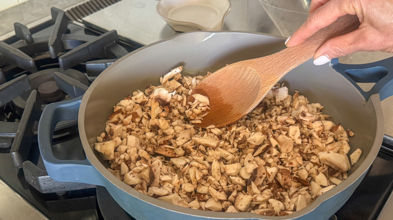 Wooden spoon stirring chopped mushrooms in skillet