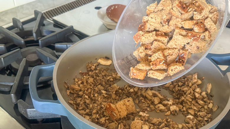 cubed bread going into skillet with mushrooms