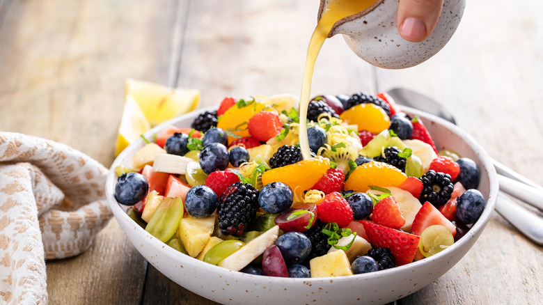 Pouring dressing over a bowl of mixed fruit