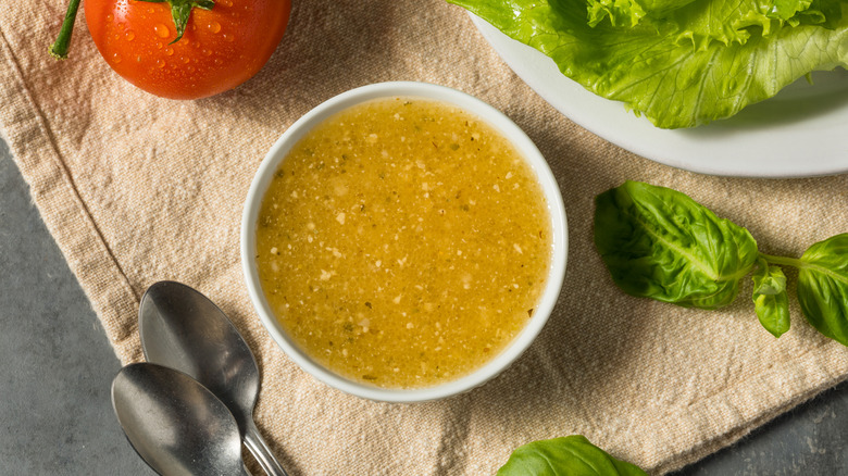Bowl of Italian dressing next to tomatoes and salad