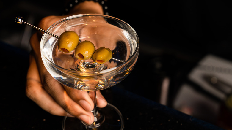 A person holds a classic martini cocktail with olive garnish