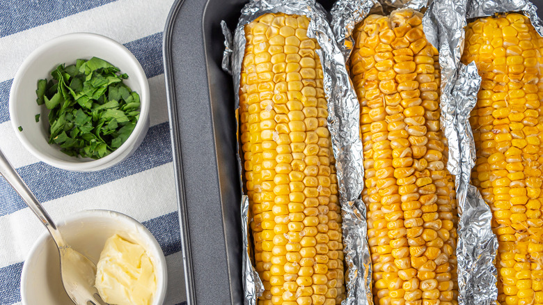 Oven-baked corn on the cob wrapped in aluminum foil with butter and herbs