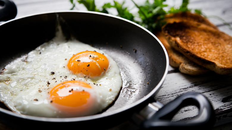 Two fried eggs in nonstick pan with some toast on the side.