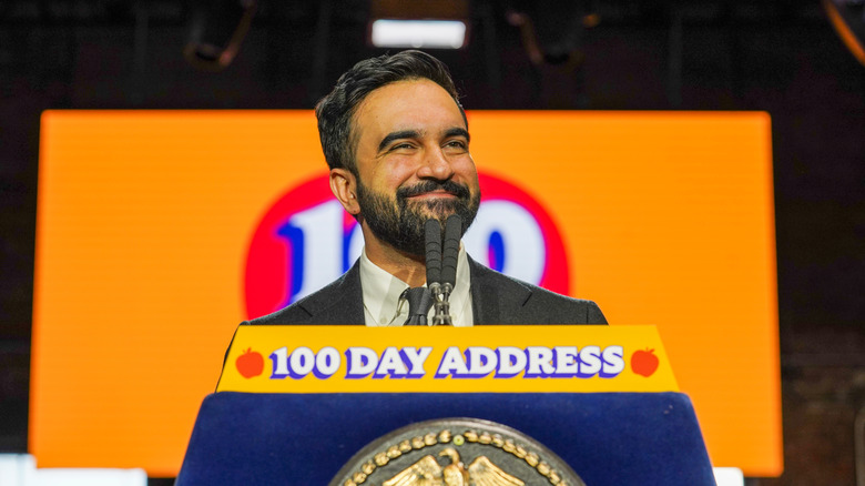 Mayor Zohran Mamdani smiling at the podium as he delivers his 100 Day Address in New York City