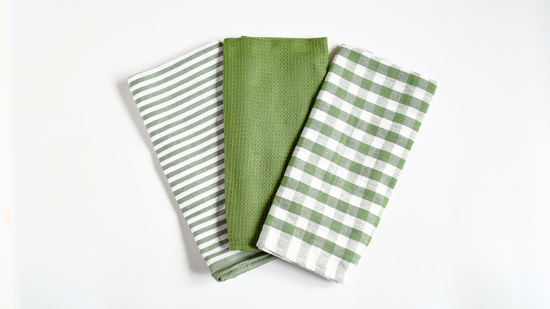Three green colored folded kitchen towels against a white background