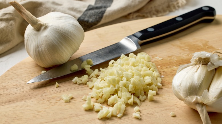 Fresh garlic being cut on a small wooden board