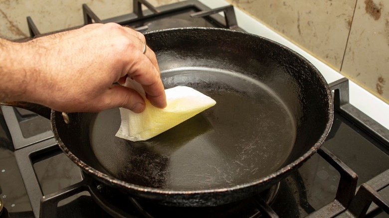 A hand wiping oil from a cooking pan with a paper towel.