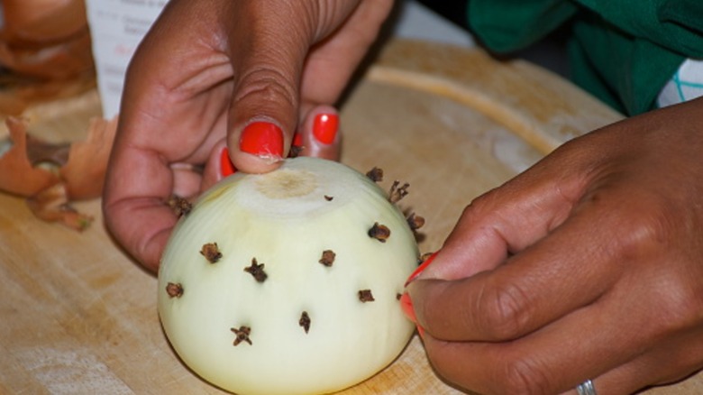Hands putting cloves in onion half