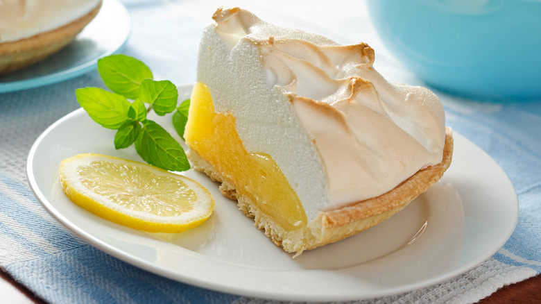 Slice of lemon meringue pie on plate with lemon slice and mint