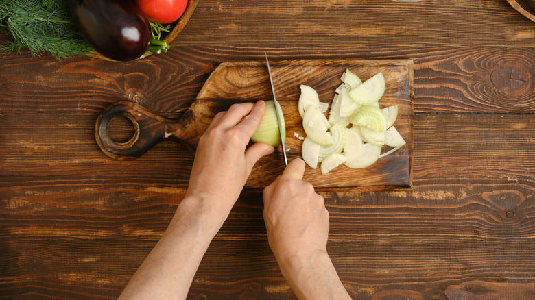 An onion on a smal wooden board being chopped, shot from above