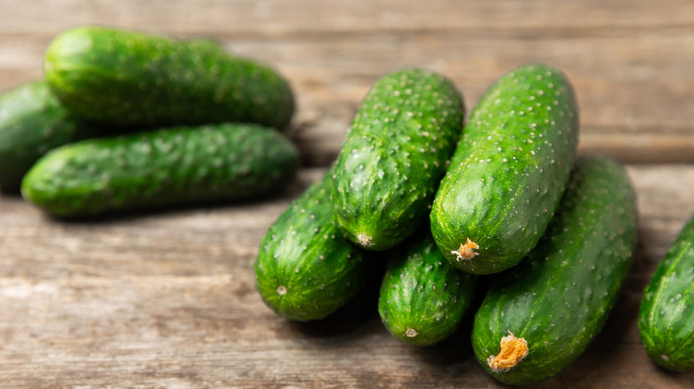Two piles of cucumbers on a wooden surface.