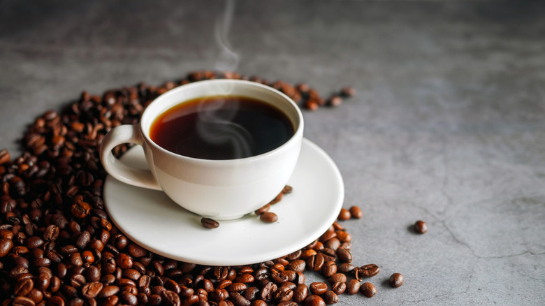 A cup of coffee and a pile of coffee beans sitting on a table.