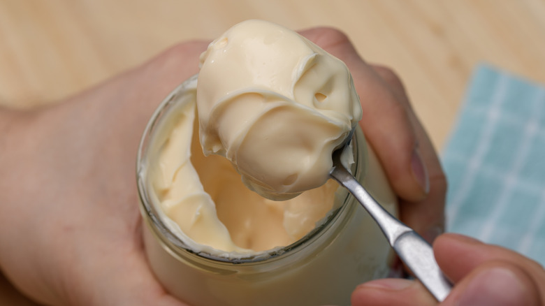 Hand holding jar of mayonnaise with spoonful