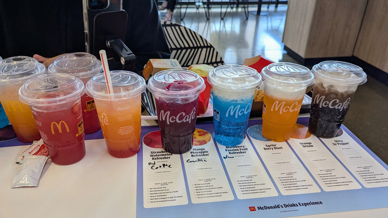 Tasting lineup of six brightly colored beverages on table.