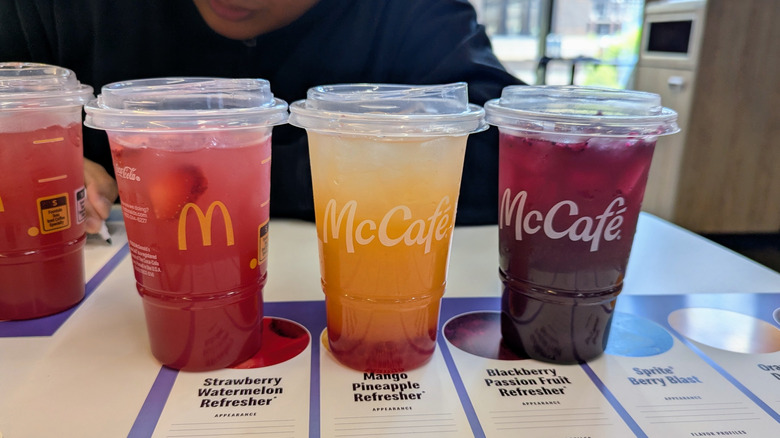 Three McDonald's Refresher drinks on a table, including strawberry-watermelon, mango-pineapple, and blackberry.