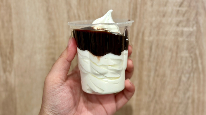 Someone holding a McDonald's sundae in their hand in front of a wood panel wall.