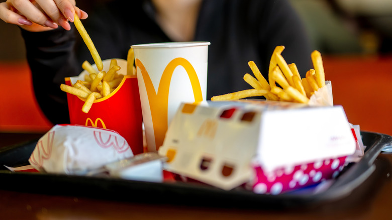 A woman takes a french fry from a tray of McDonald's food in paper wrappers and containers