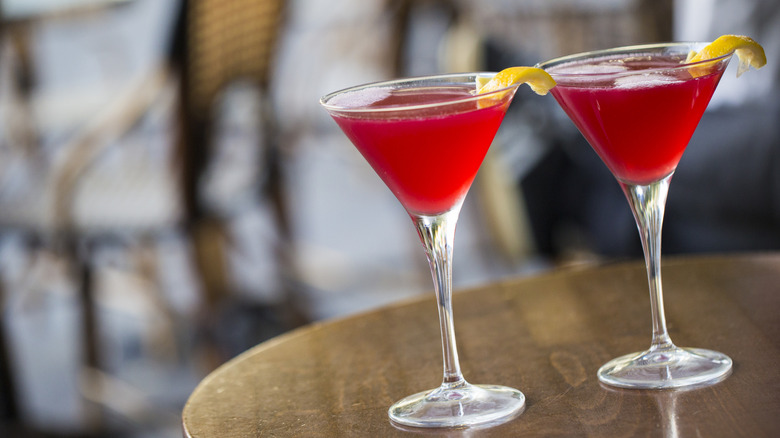 Two Cosmopolitan cocktails sit on a wooden bar