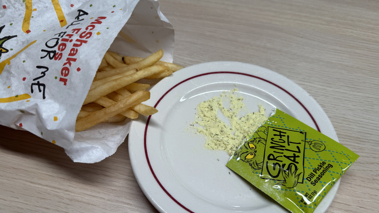The Dill Pickle Grinch Salt packet open on a plate next to fries