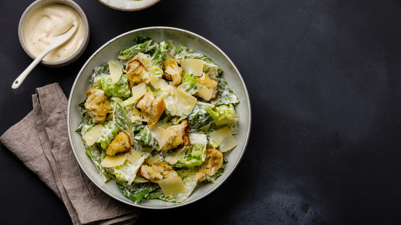 Caesar salad in a bowl with small bowl of Caesar dressing on the side.