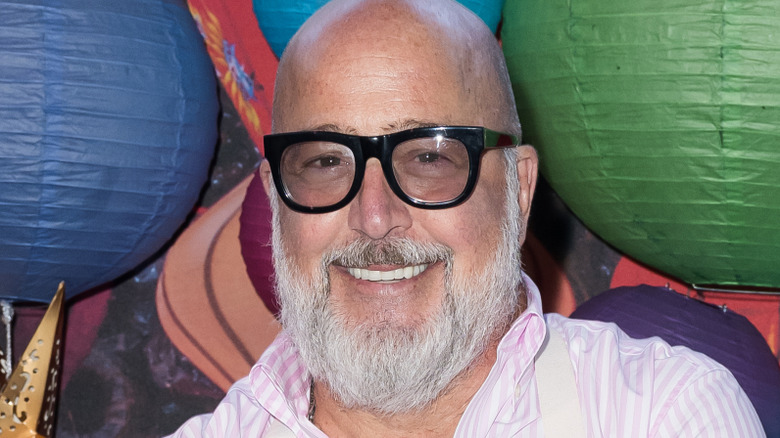 Andrew Zimmern smiles and wears glasses at an event