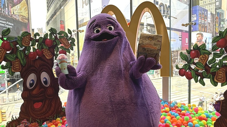 Grimace holds the McDonaldland meal and shake in his hands, while standing in a ball pit at a McDonald's in Times Square