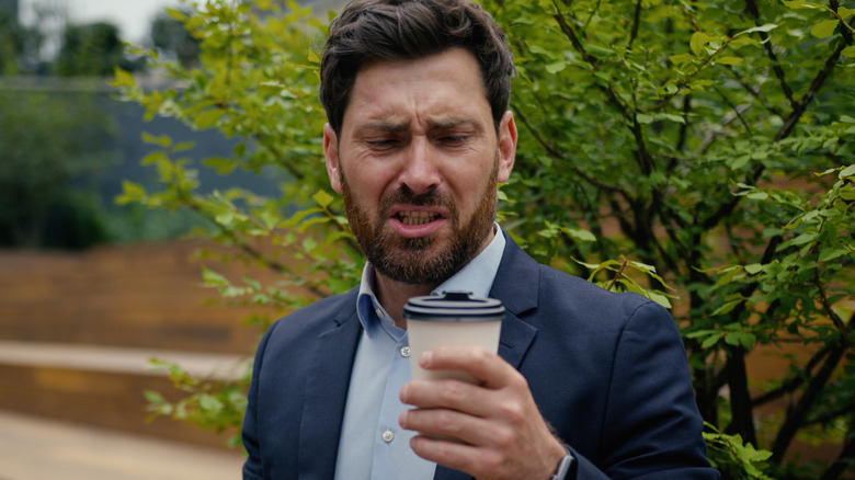 Man in suit outside looking disgusted at his to-go coffee