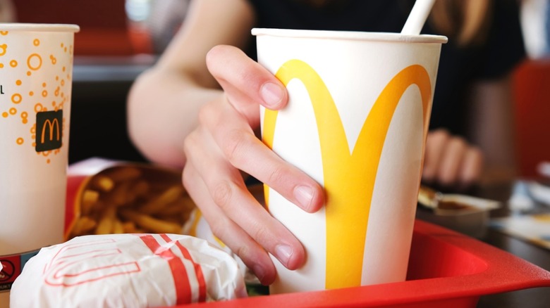 A hand holding a McDonald's drink cup on a tray with a meal.