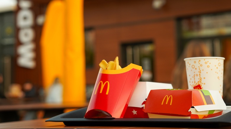 A McDonald's meal with fries, soda, and burger in boxes in front of a McDonald's restaurant