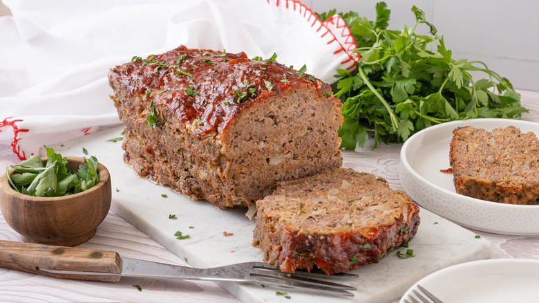 ketchup and parsley-topped meatloaf on a white board posed next to a pile of parsley