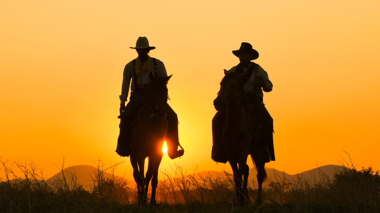 Two cowboys riding on horses against a sunset
