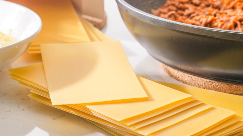 Uncooked lasagna noodles laid out next to meat sauce.