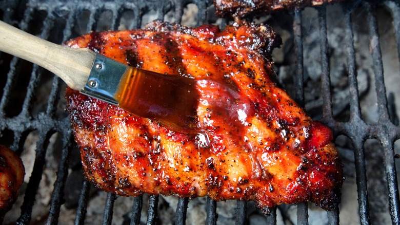 Half rack of baby back pork ribs being basted with sauce on grill