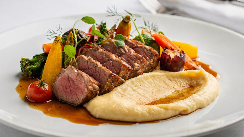 Medium-rare beef with mashed potatoes on a white plate.