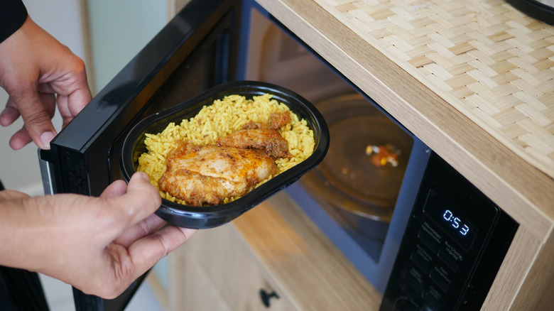 A dish of chicken and rice being removed from a microwave