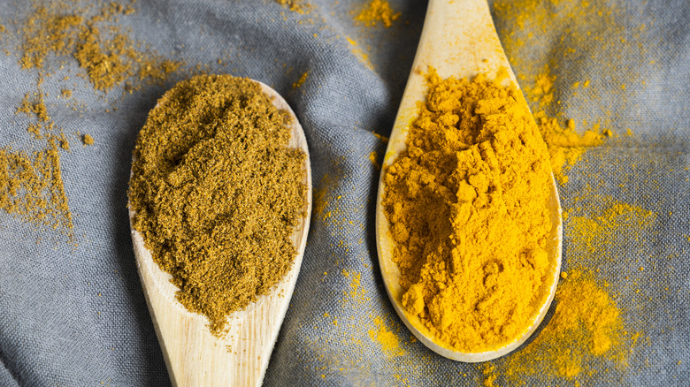 Two wooden spoons filled with ground cumin and turmeric