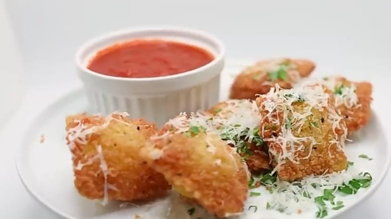 Toasted Ravioli on white plate, tomato sauce behind
