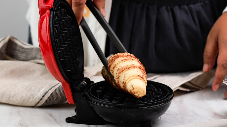 Person placing croissant on mini waffle maker