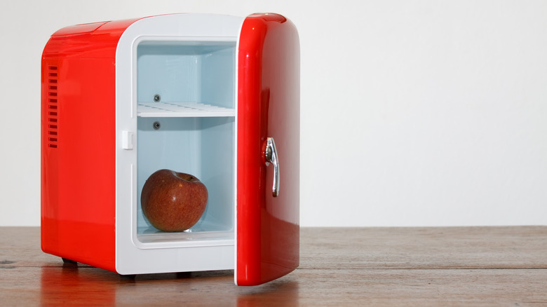 A red countertop mini-fridge with the door open and a red apple inside