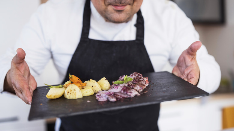Proud chef holding a plate consisting a meat dish along with vegetable side dish