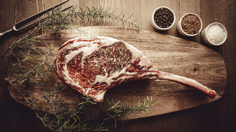 Raw dry aged Wagyu tomahawk steak on a wooden platter