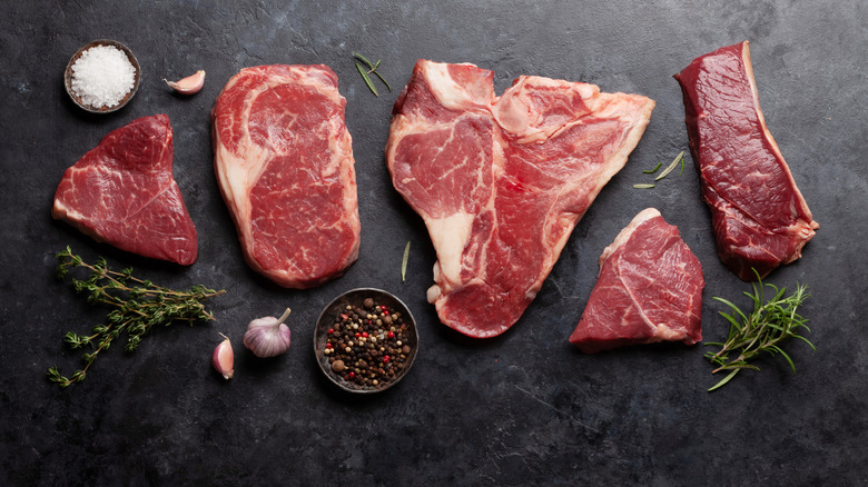 Various raw beef steaks with herbs and spices. Top view flat lay