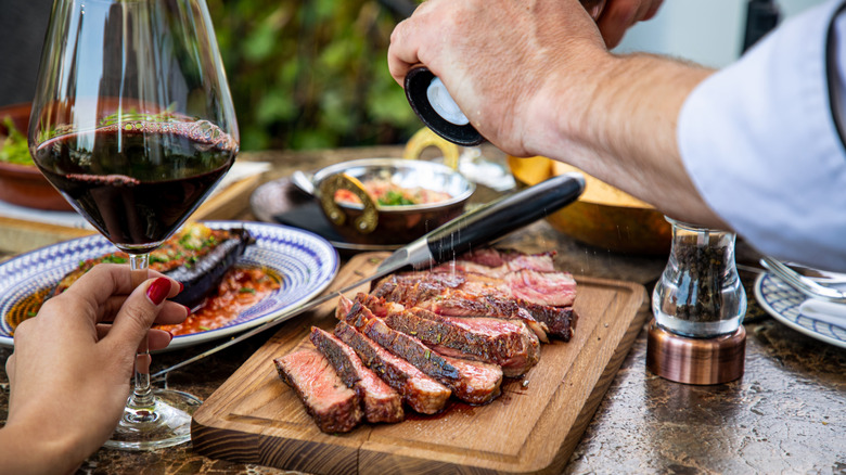 Seasoning juicy medium rare beef steak with salt grinder, cut on wooden board on restaurant table