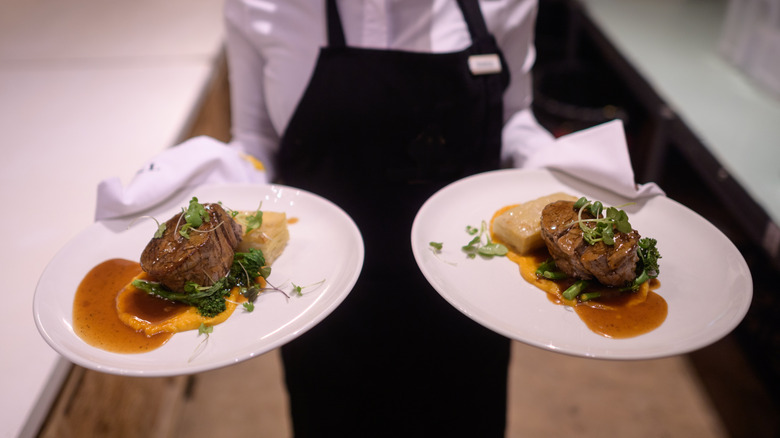 Waiter holding hot plated grilled steak and vegetables potatoes asparagus butter nut garnish sauce