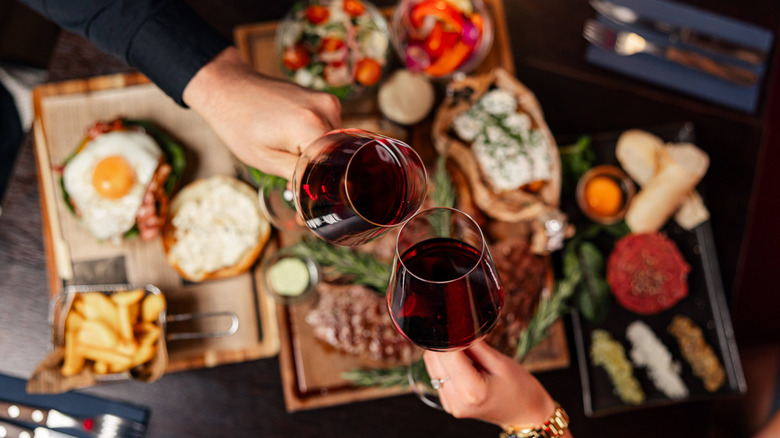 Clinking red wine glasses over a gourmet steak dinner