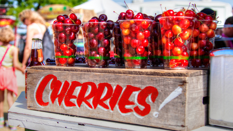 A wooden box painted with the word cherries topped with plastic glasses full of a variety of cherries