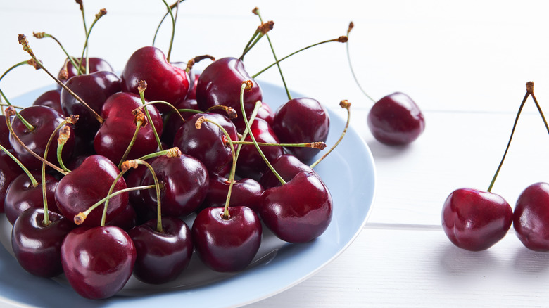 Red Ripe Cherries On A Ceramic Plate, On A White Wooden Table.