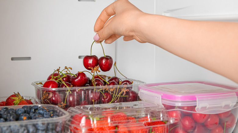 Woman taking cherry in plastic container from refrigerator, closeup