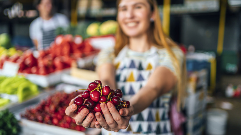 Smiling market vendor showing cherries to a customer